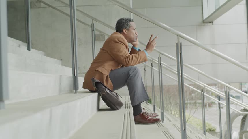 A man talks on a phone while sitting on concrete steps