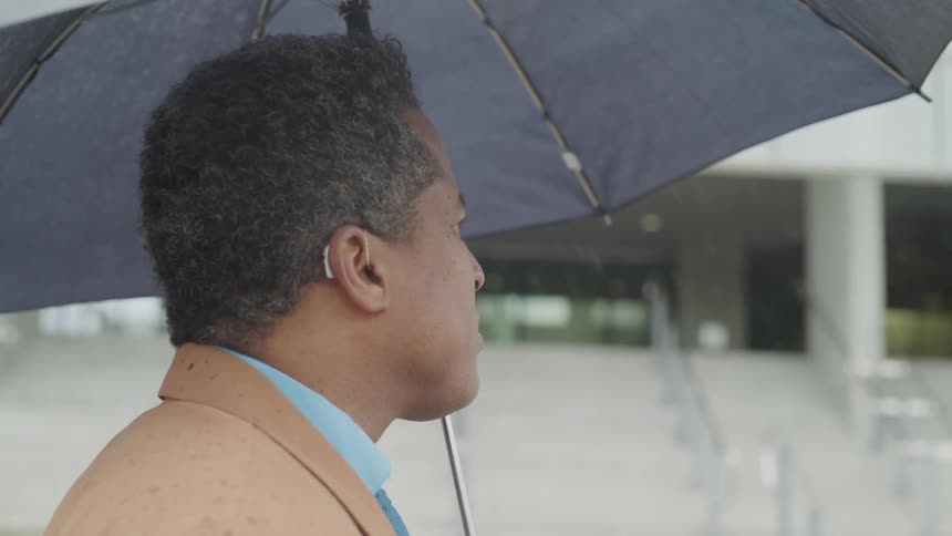 A man standing under the rain holding an umbrella