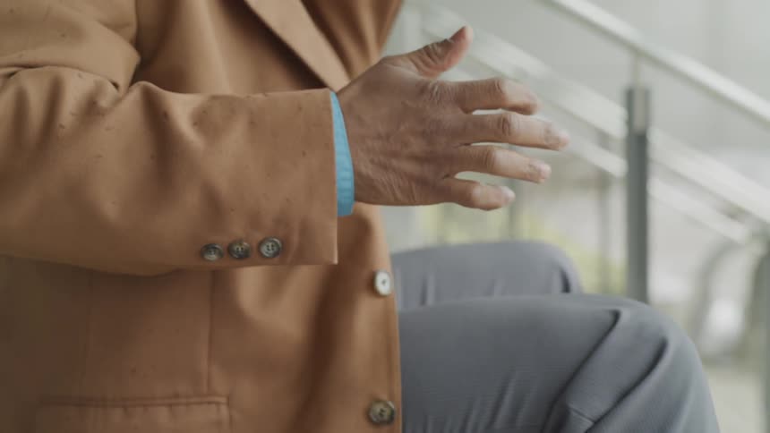 Man in suit sits on stairs and talks on phone while waving hand