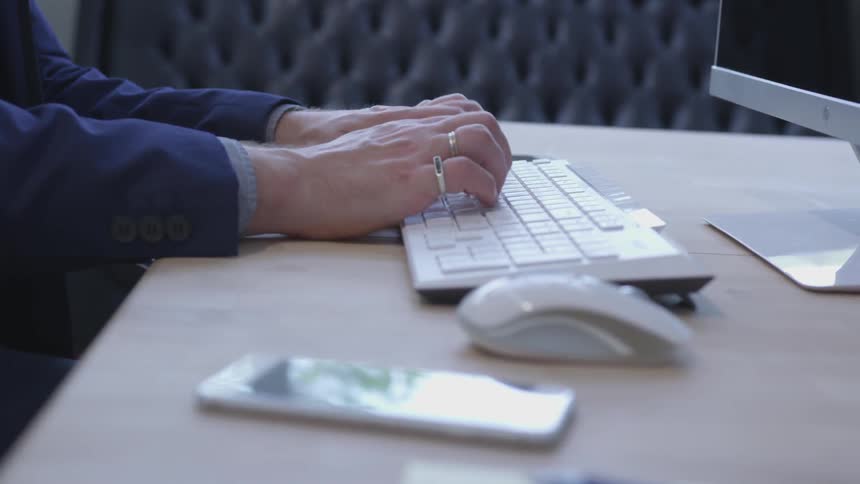 A man types on a keyboard while sitting at a desk