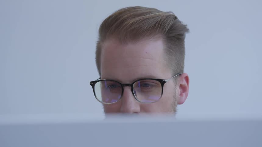 Man wearing glasses looks at monitor in pale room