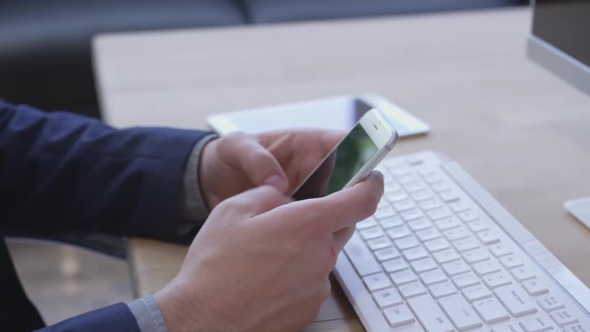 Man typing quickly on a phone while sitting at a work table