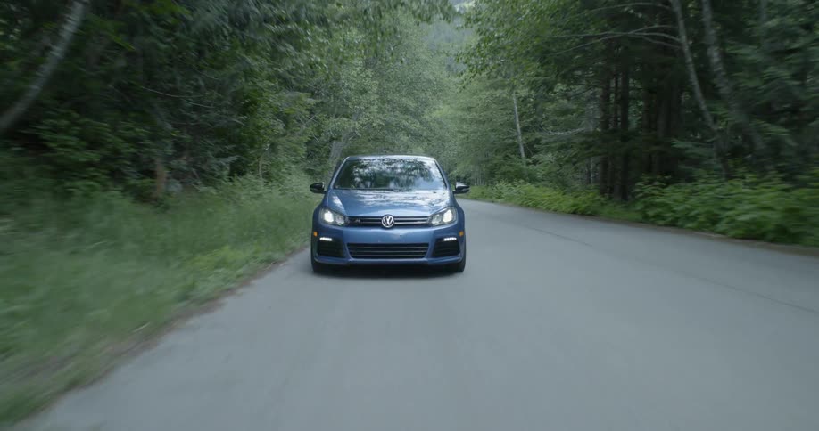 A blue volkswagen travels on a forest road
