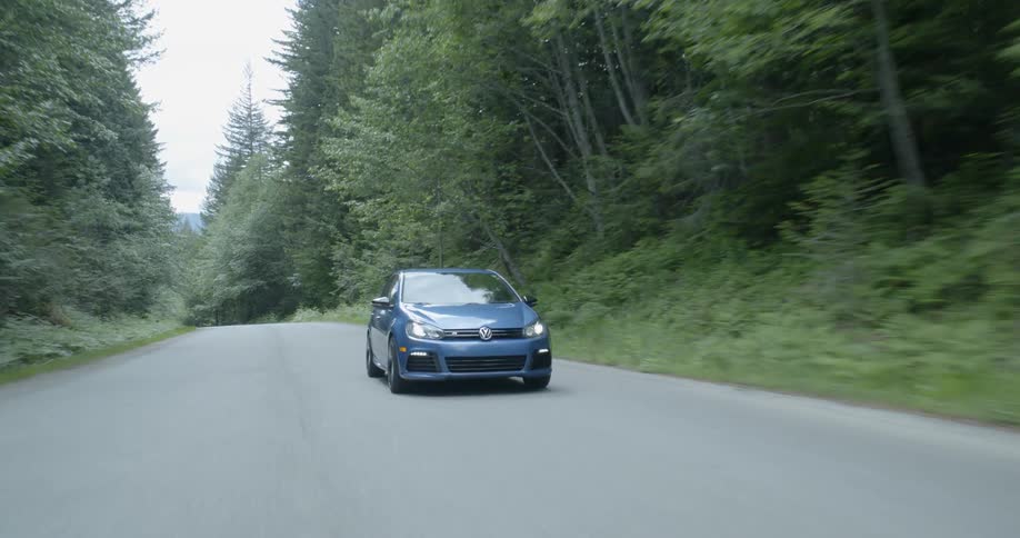 A blue car drives down a road in the forest