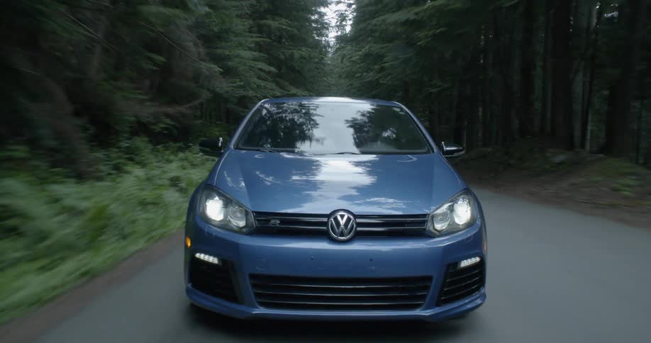 A blue volkswagen travels on a forest road