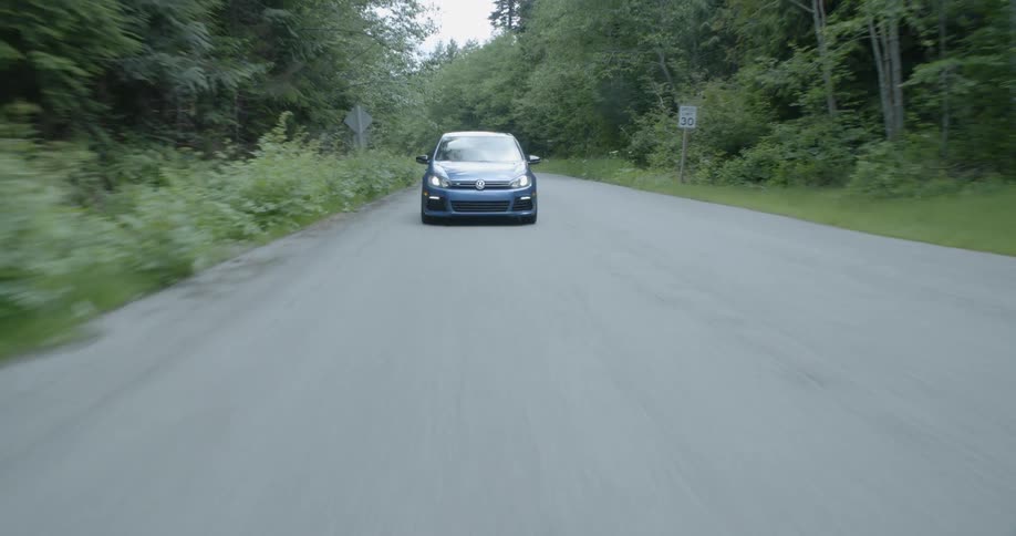 Blue car drives down road with trees on either side