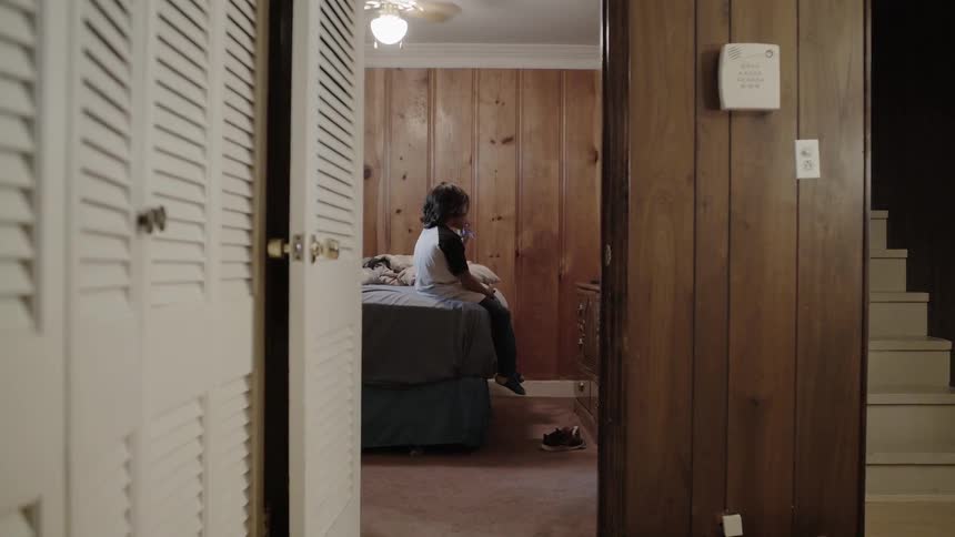 A boy sitting on a bed in a bedroom at daytime