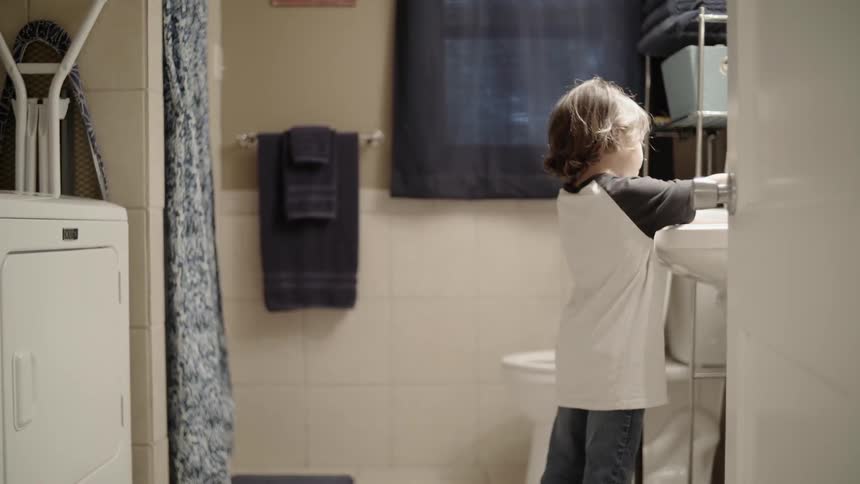 A boy fills a glass up with water from the sink