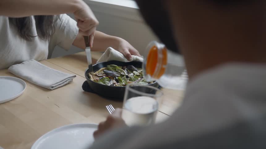 Woman is cutting a slice while man is pouring a drink
