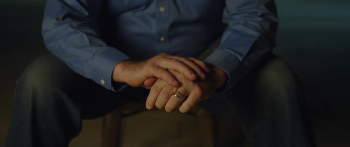 A man's hands fidget while he sits on a stool