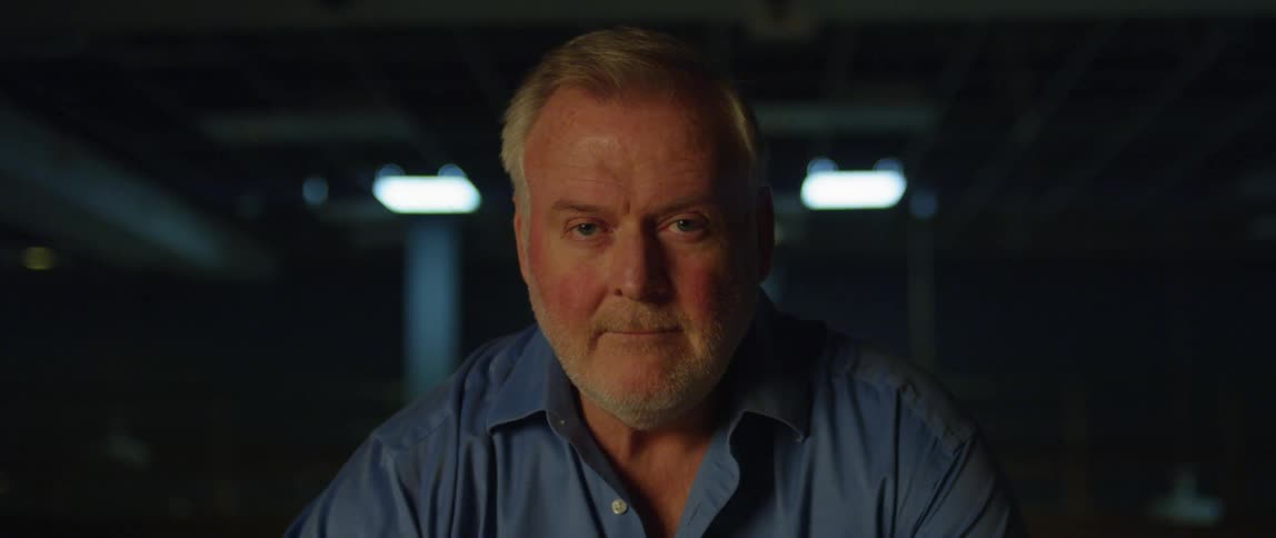 Man stares with a grim face in dimly lit room