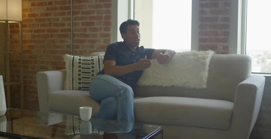 Man sits on a couch talking and gesturing