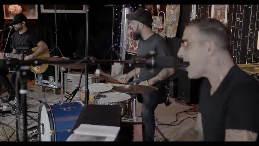 A band with a drummer guitar player and keyboardist singing in a room