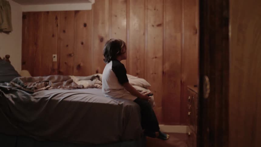 Boy sitting on bed alone in a room watches tv
