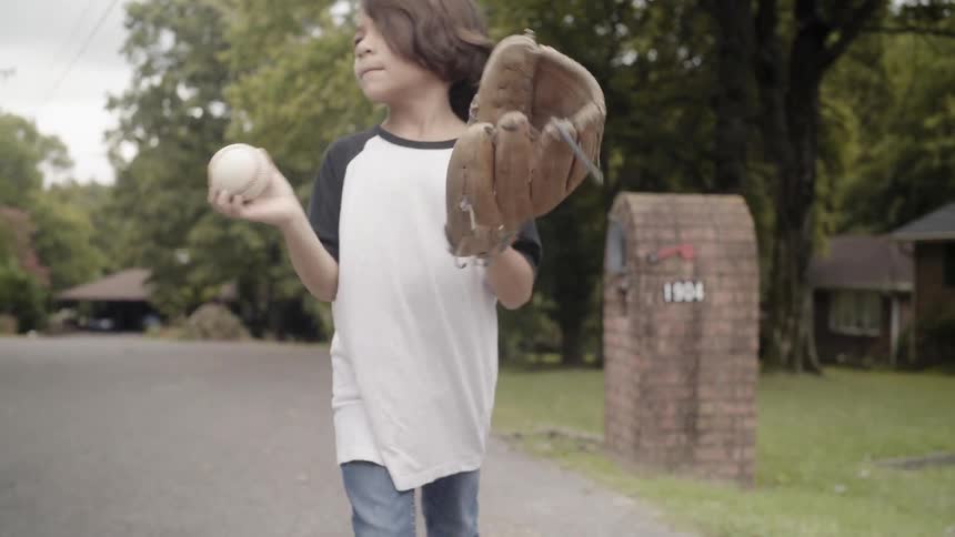 Boy holding baseball and glove walks down a rural road