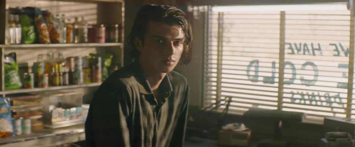 A man stands in a bright room next to a window with horizontal blinds