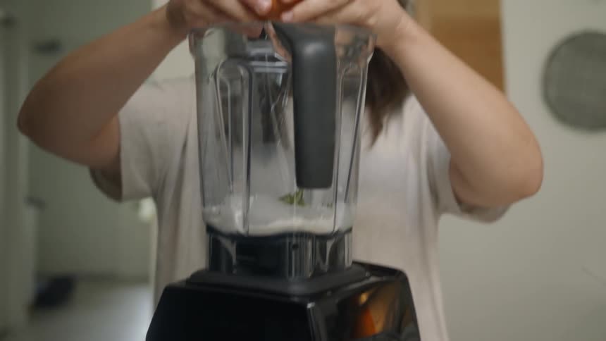 A woman adds an egg to a blender