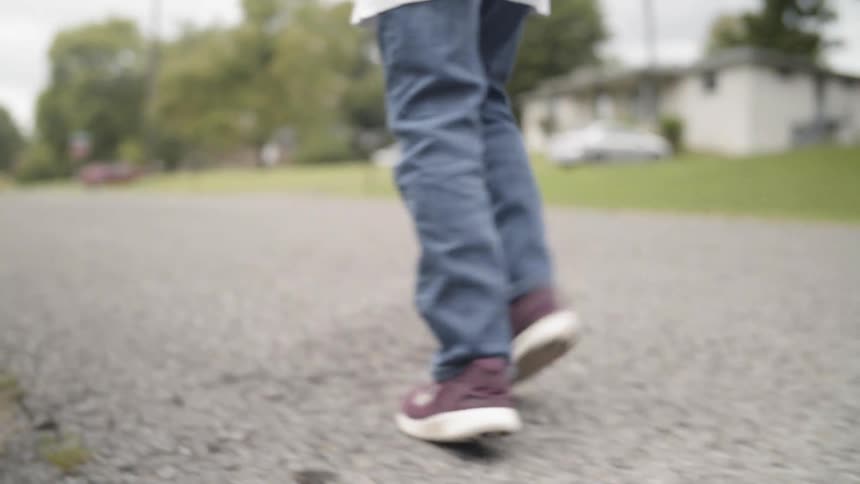 A boy walks on a sidewalk while holding a baseball glove
