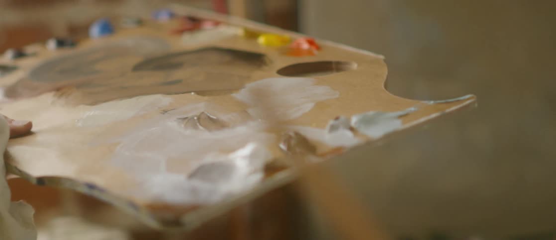 An artist holding a paint palette and brushing on a canvas