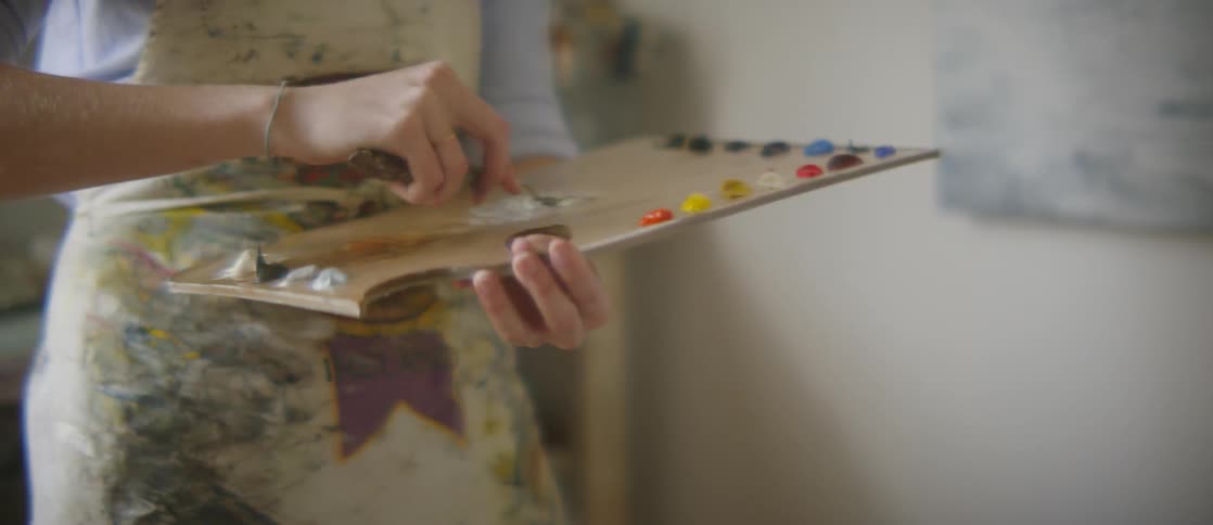 A person mixes white paint on a painter's board