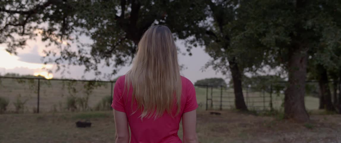A woman in a pink shirt walks towards the fence