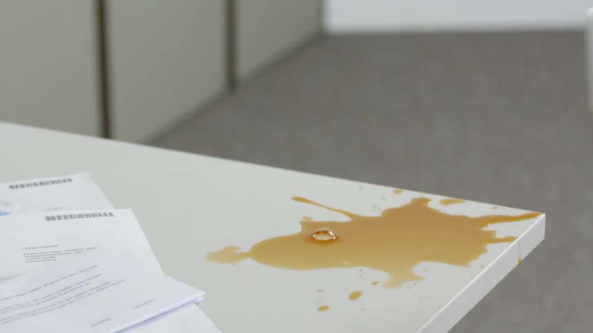Hand picks up coffee cup on table with coffee spilled around it