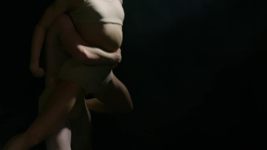 Two dancers perform a move under a spotlight in which the female dancer is lifted by the male