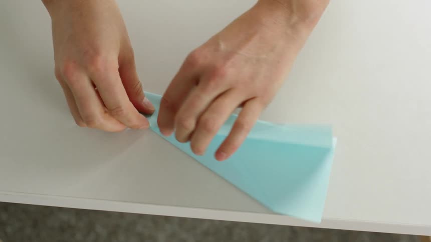 A person folding a piece of light blue paper into a paper airplane