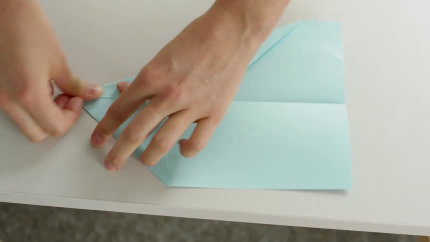 Hands fold a paper airplane on a white table