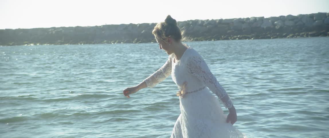 A woman is splashing around on the beach in a white dress