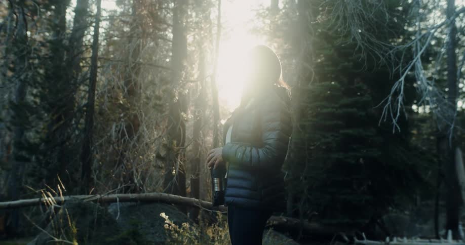 A woman with a jacket on stands in a forest