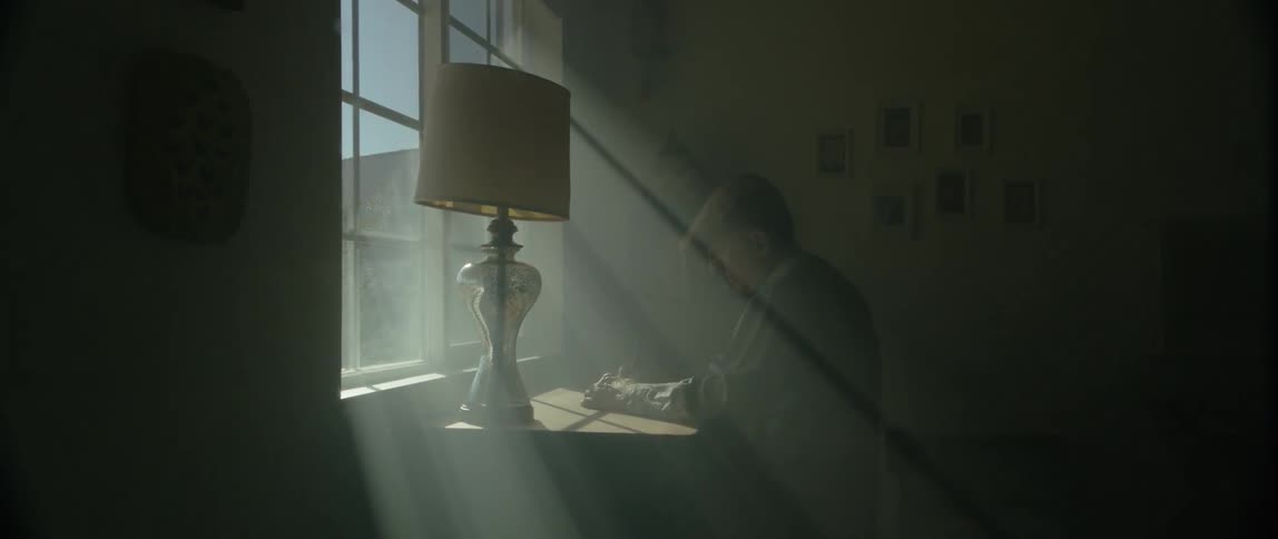 Light streams through a window onto an old man sitting at a table