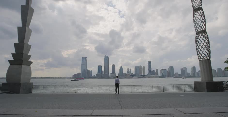 A man stands by the water looking towards the city