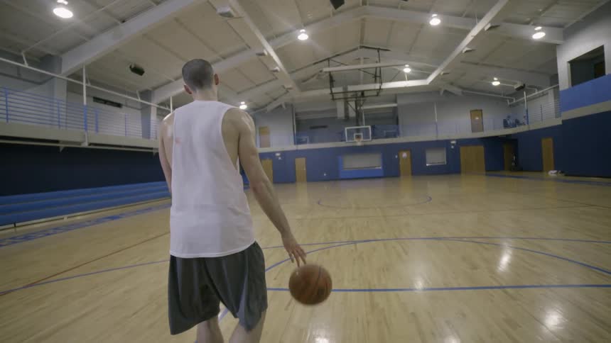 A man dribbles a basketball on an interior basketball court