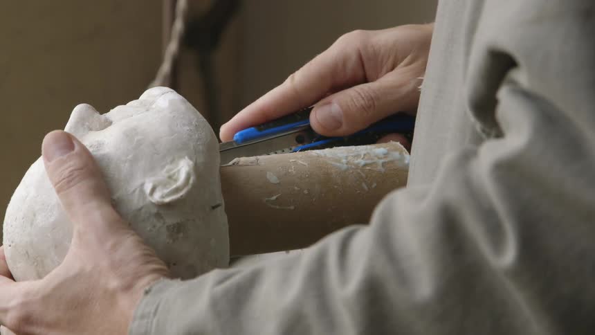 A man carving a piece of wood that is attached to a carved head