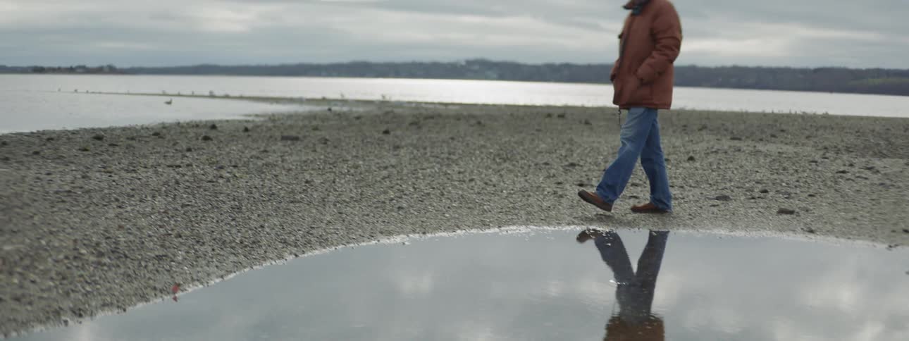 A man strolls by a puddle on an overcast day