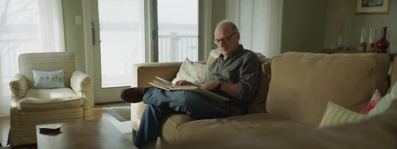 Elderly man sits on a couch looking at a photo album