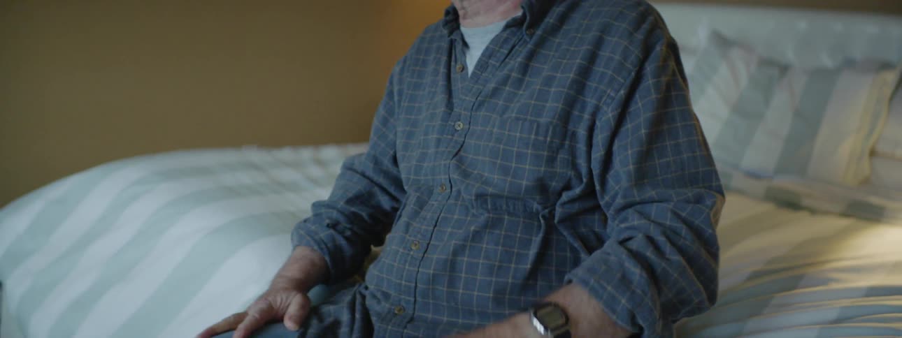 Older man putting on a wristwatch and standing up from bed