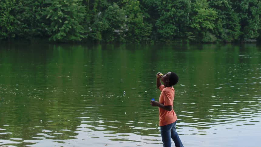 A child blows bubbles by the lake
