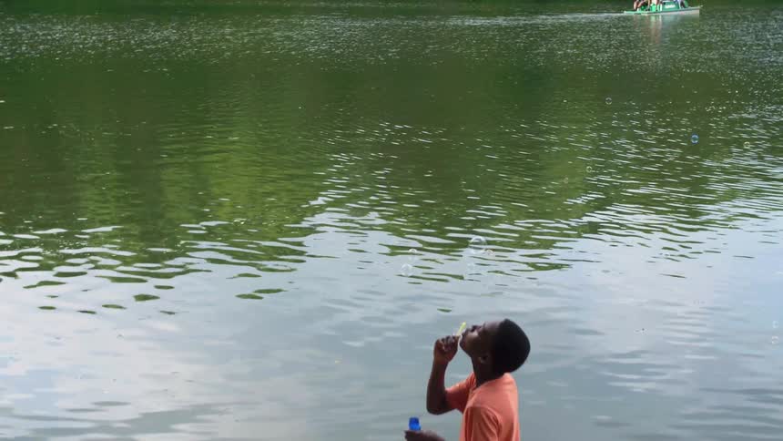 A boy blows bubbles while standing by a lake
