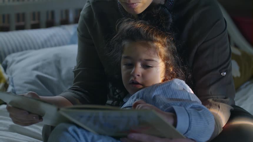 A woman is reading from a book to a child in bed