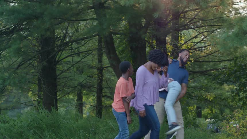 A mother daughter father and son walking through a park with the little girl riding piggyback on dad