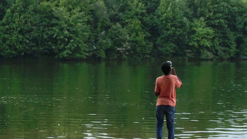 A boy blows bubbles on a lakeshore