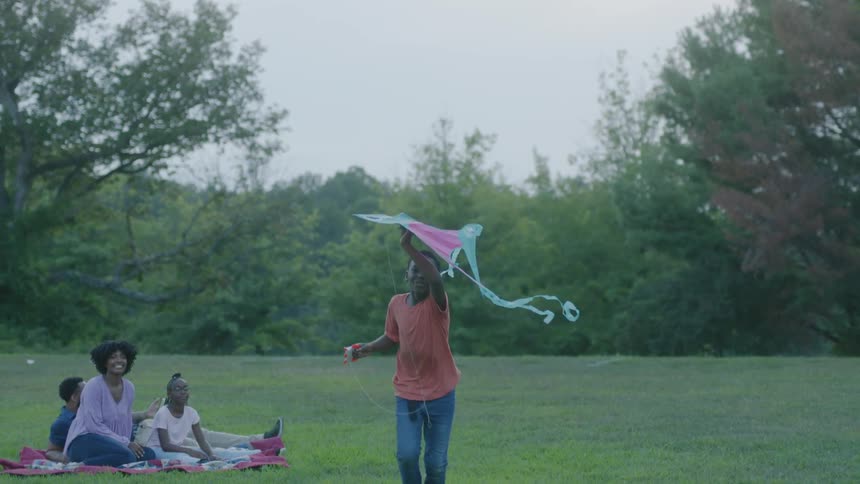 A young boy flies a kite while his sister mom and dad watch