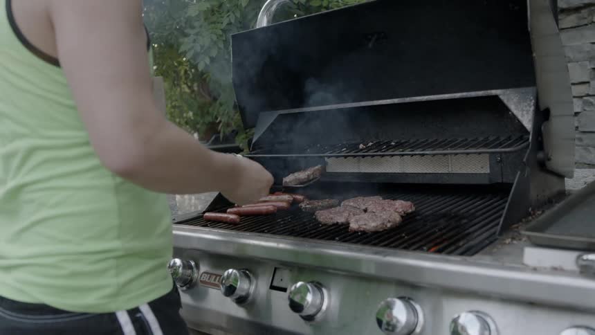 A man stands at a grill flipping burgers with a spatula