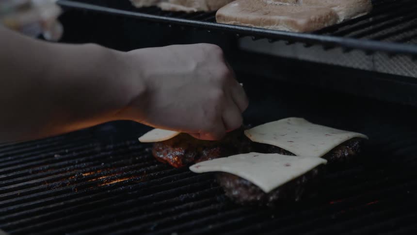 Man puts some cheese on burger while grilling