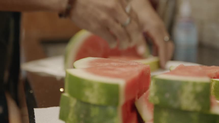 A woman wearing a lot of rings and bracelets cuts large pieces of watermelon