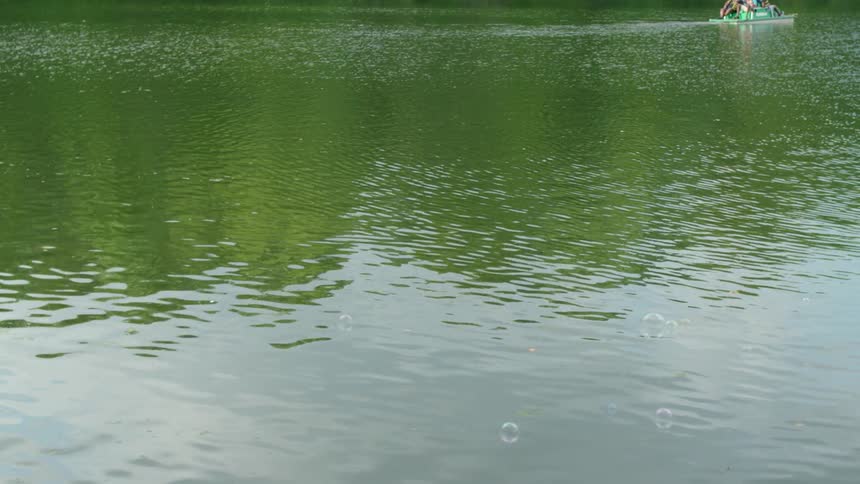 A boy blows bubbles which float out over the lake