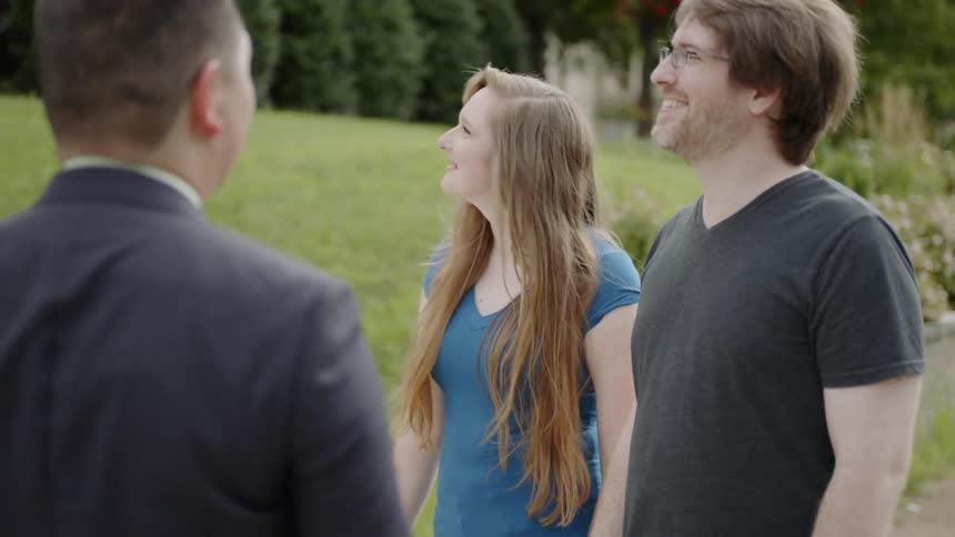 Man shakes hand with man and woman smiling outside by daytime