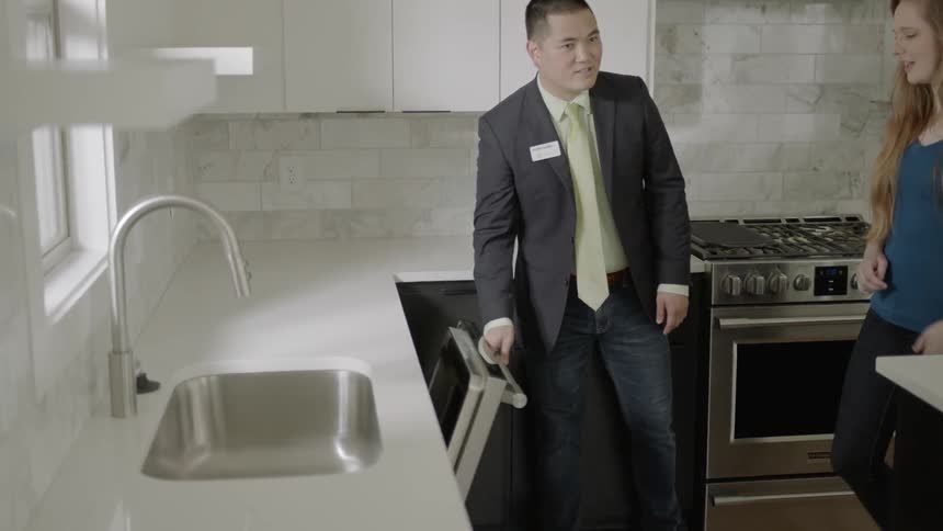 Man shows the oven to man and woman in kitchen by daytime